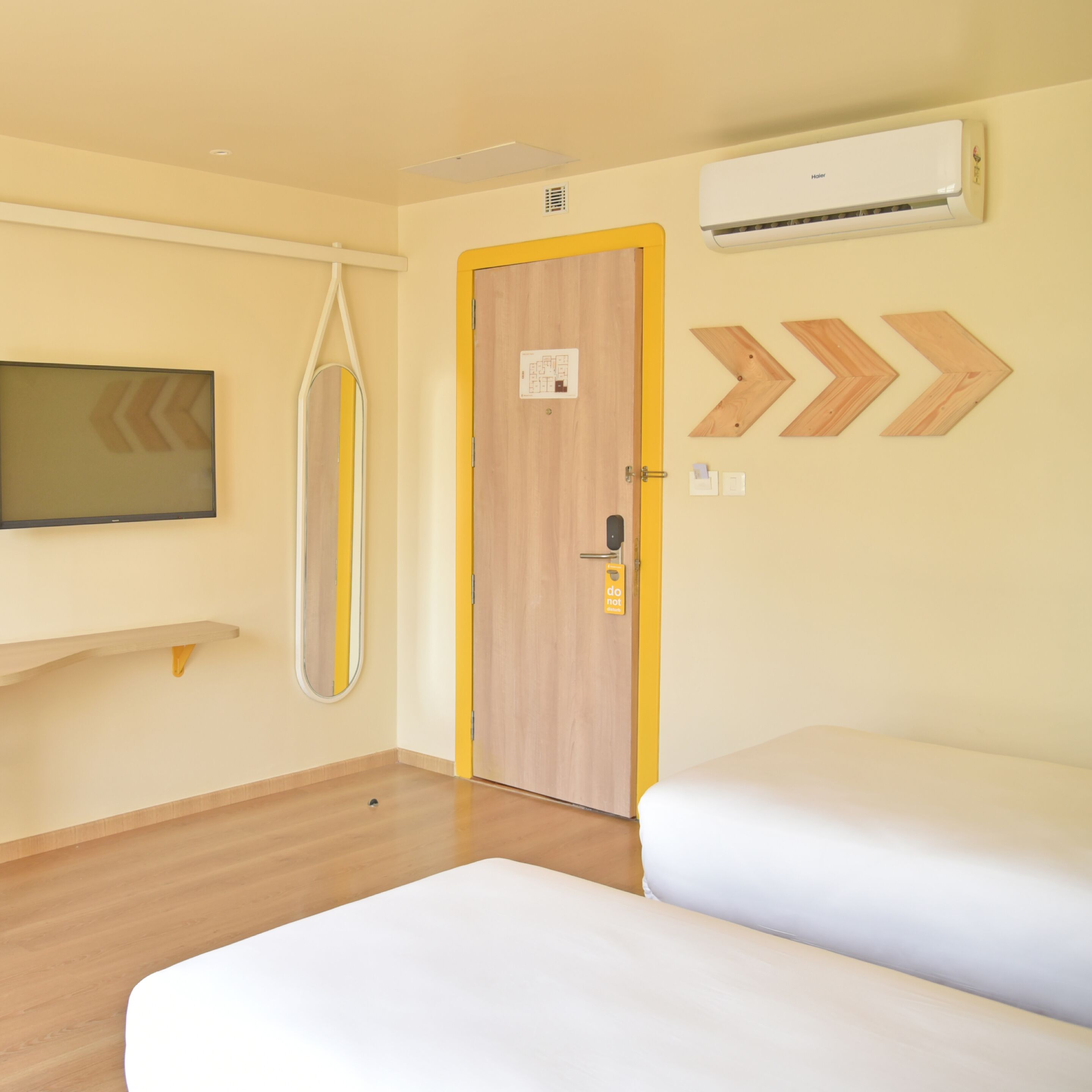 Ein Hotelzimmer mit Holztür, einem montierten Fernseher, einem Schild mit der Aufschrift ‚Bitte nicht stören‘ und einer Wand-Klimaanlage.