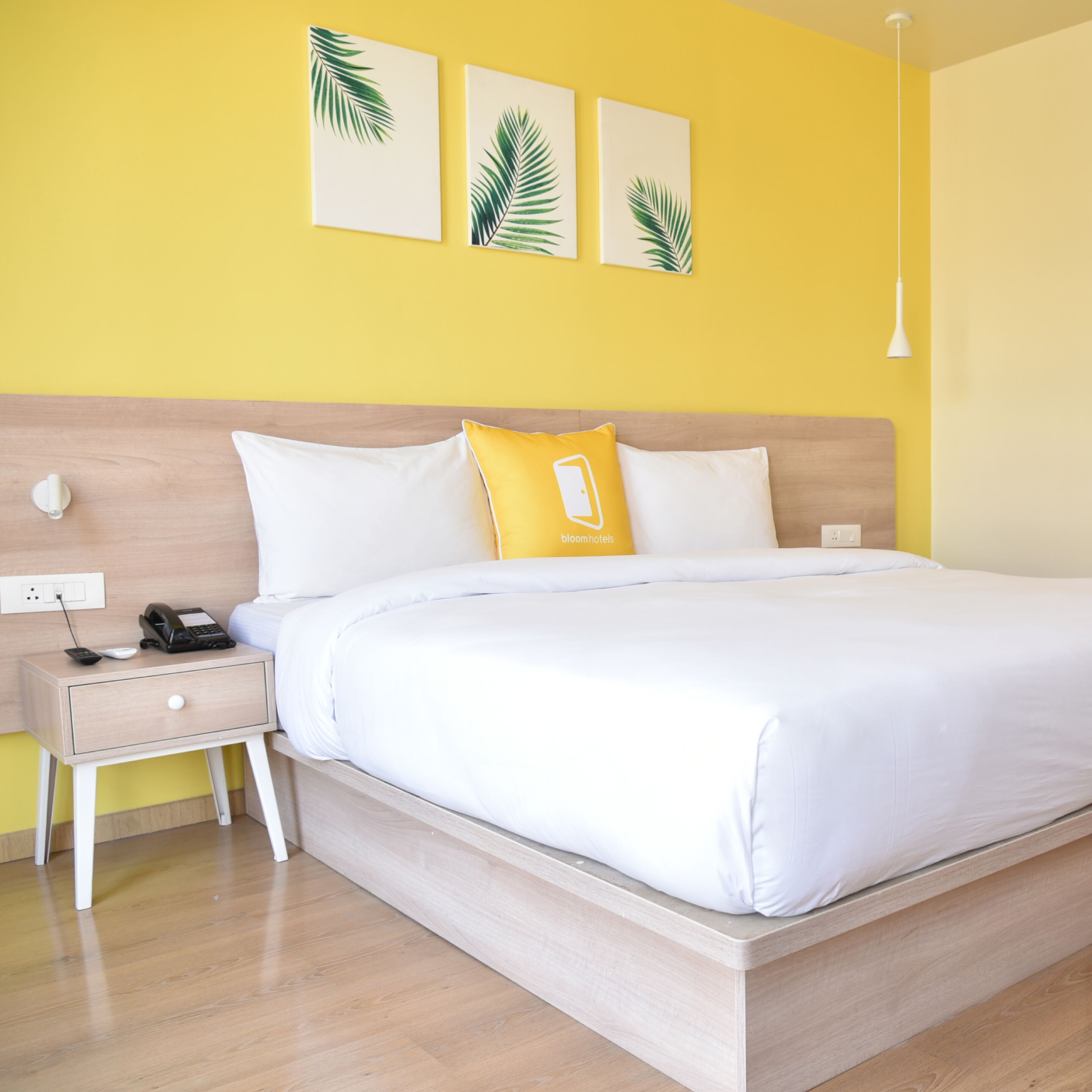 A neatly made bed with white bedding, a wooden headboard, and a nightstand with a phone and remote control.