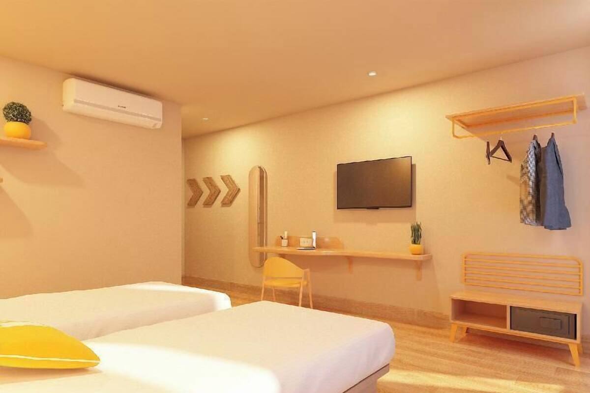 Habitación de hotel con dos camas, un escritorio, una silla, un televisor y una estantería con ropa y una planta.