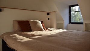 A bedroom with a large bed, a sloped ceiling, and a window with a view of trees. - Guesthouse with jacuzzi in picturesque Leiedorp (Zulte)