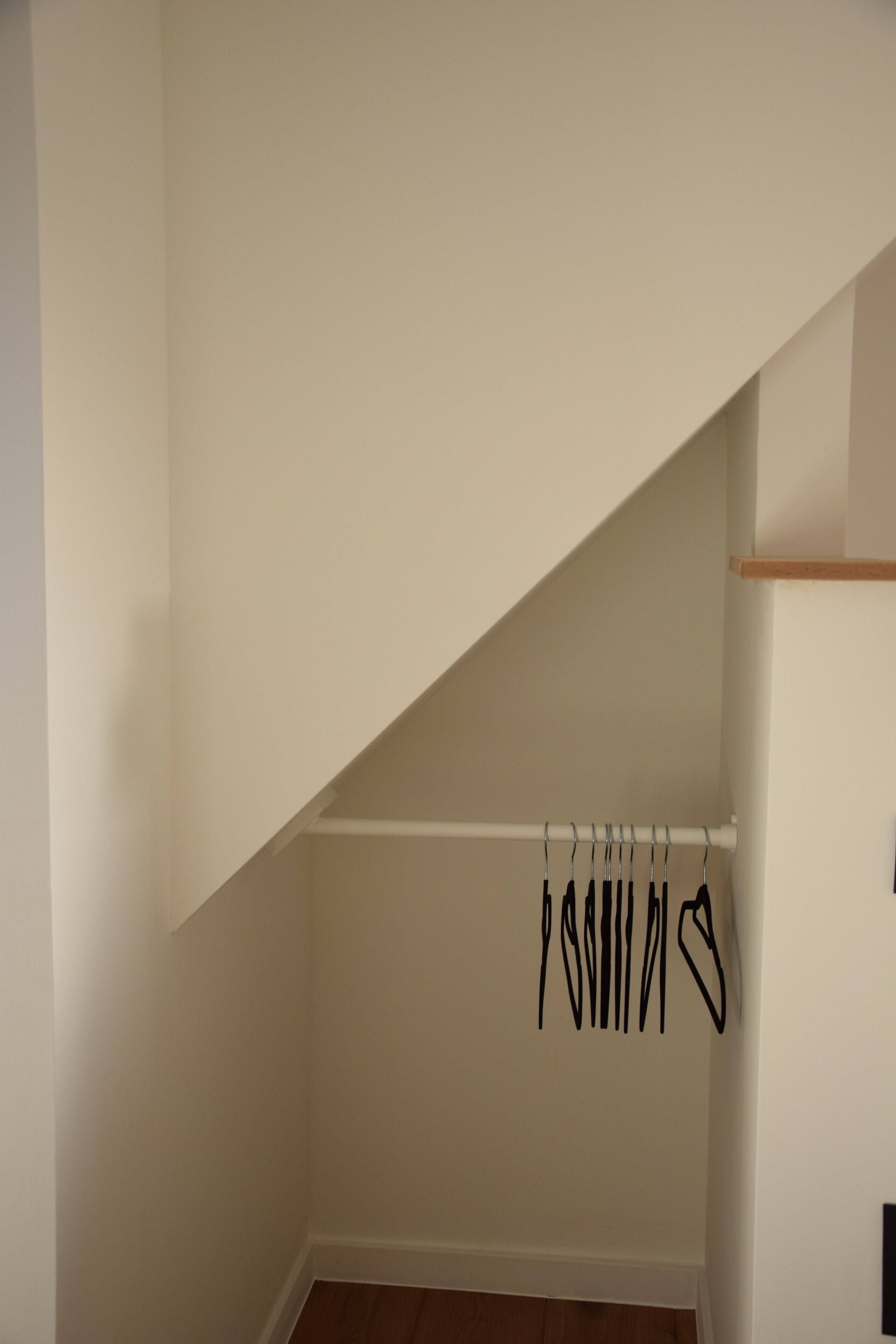 Canto de um quarto com parede branca, assoalho de madeira e teto branco. Há uma viga branca atravessando o teto, e um objeto preto pendurado nela.