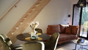 A modern loft-style room with a dining area featuring a round table and chairs, a sofa, and a small side table with a vase. - Guesthouse with jacuzzi in picturesque Leiedorp (Zulte)