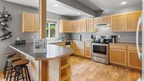 Una cucina moderna con mobili in legno, un'isola centrale con sgabelli, elettrodomestici in acciaio inossidabile e una cantinetta a parete.