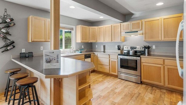Una cocina moderna con armarios de madera, una isla central con taburetes, electrodomésticos de acero inoxidable y una estantería para vinos en la pared.