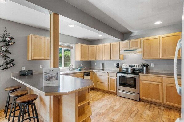 Una cocina moderna con armarios de madera, una isla central con taburetes, electrodomésticos de acero inoxidable y una estantería para vinos en la pared.