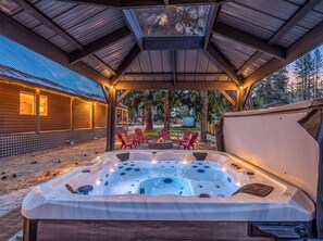 Een hottub onder een houten prieel, met uitzicht op een huis en bomen.