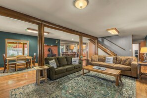 Un salon chaleureux avec une cheminée, un canapé vert, un divan en cuir marron et un tapis à motifs.