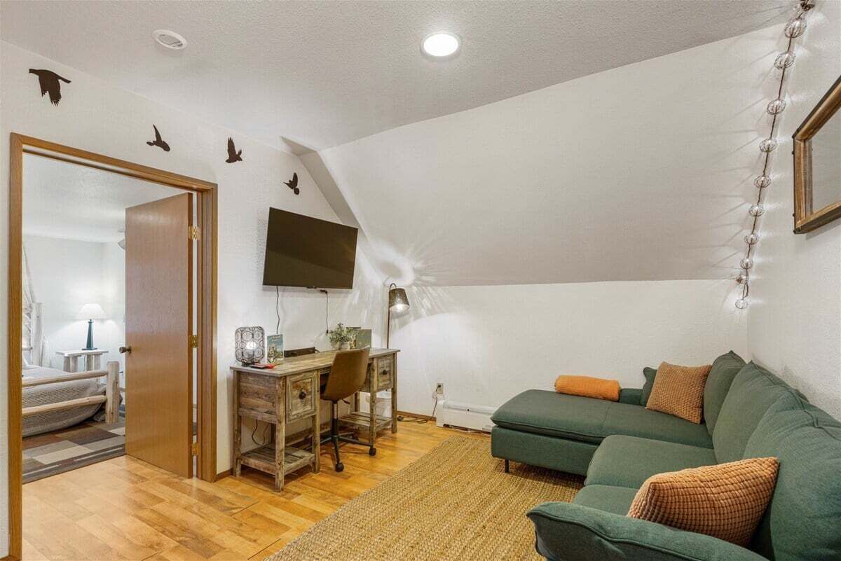 A room with a desk, a green sofa, a wooden floor, and a ceiling with a light fixture.