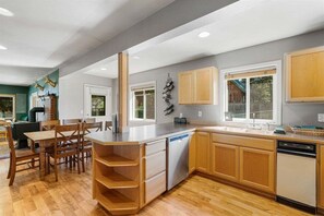 A modern kitchen with wooden cabinets, a dishwasher, and a dining area with a table and chairs.