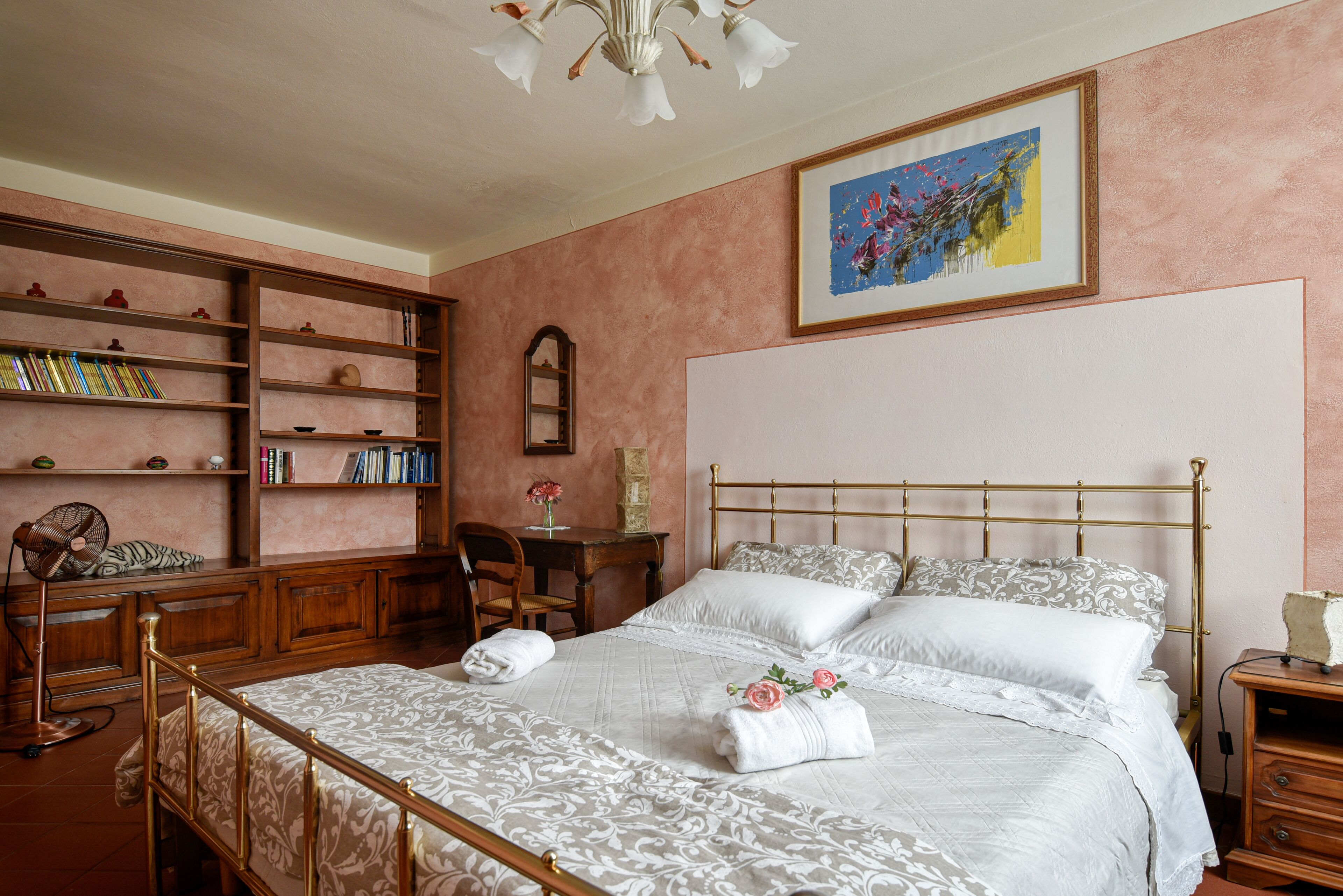 Une chambre à coucher bien rangée, avec un grand lit, un bureau en bois sur lequel sont posés des livres et une bibliothèque.