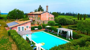 A large house with a swimming pool, surrounded by lush greenery and a clear sky.