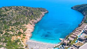 An aerial view of a coastal resort with a beach, rocky terrain, and a clear blue sea. - Etoile Villa Heated Pool (Agios Nikolaos)