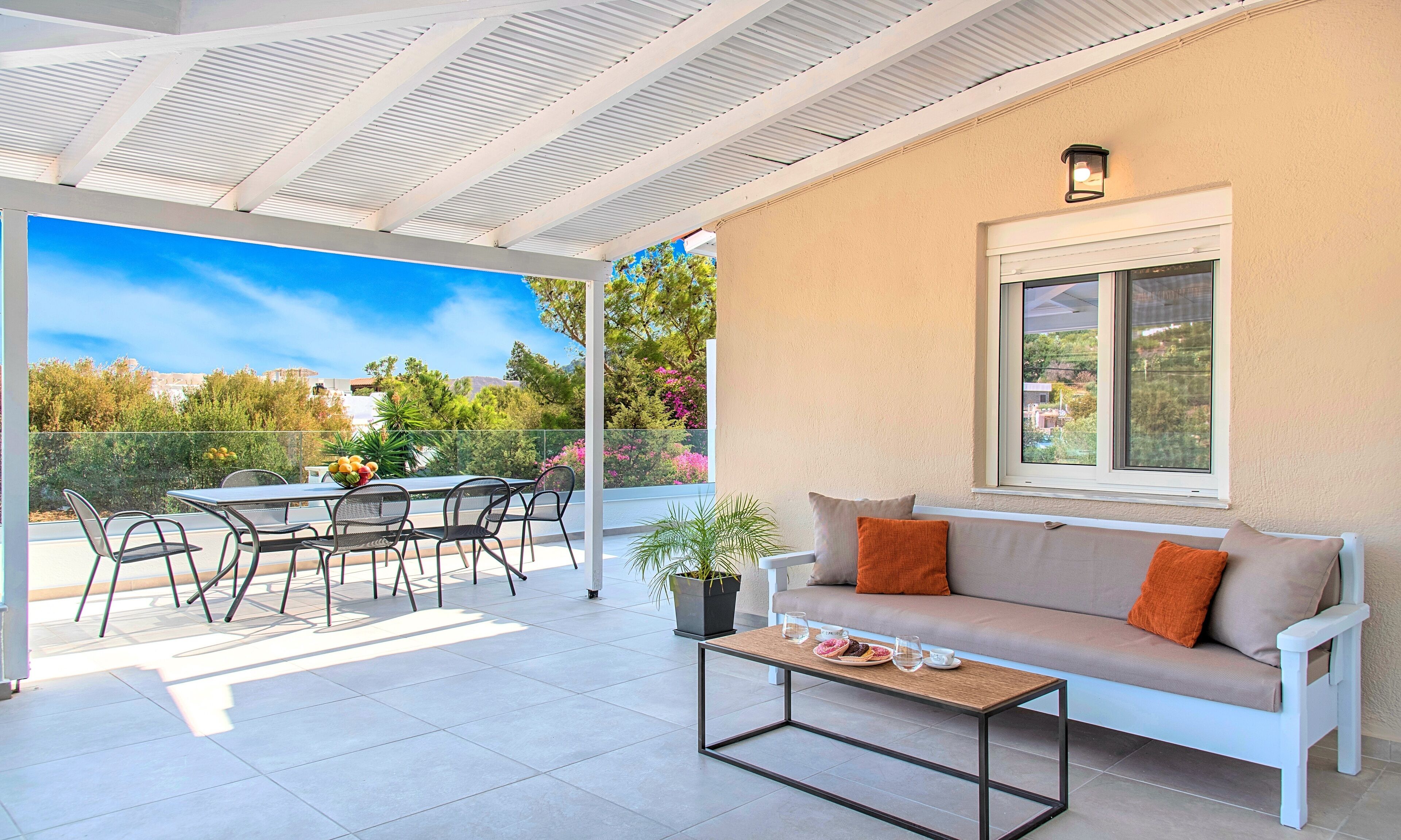 A covered patio with a table and chairs, a sofa, and a potted plant.