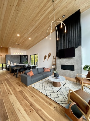 A spacious living area with a wooden ceiling, a gray sofa, a round coffee table, and a black fireplace. - Vayhaus: Contemporary cabin offering stunning views of the Smoky Mountains. (Gatlinburg)