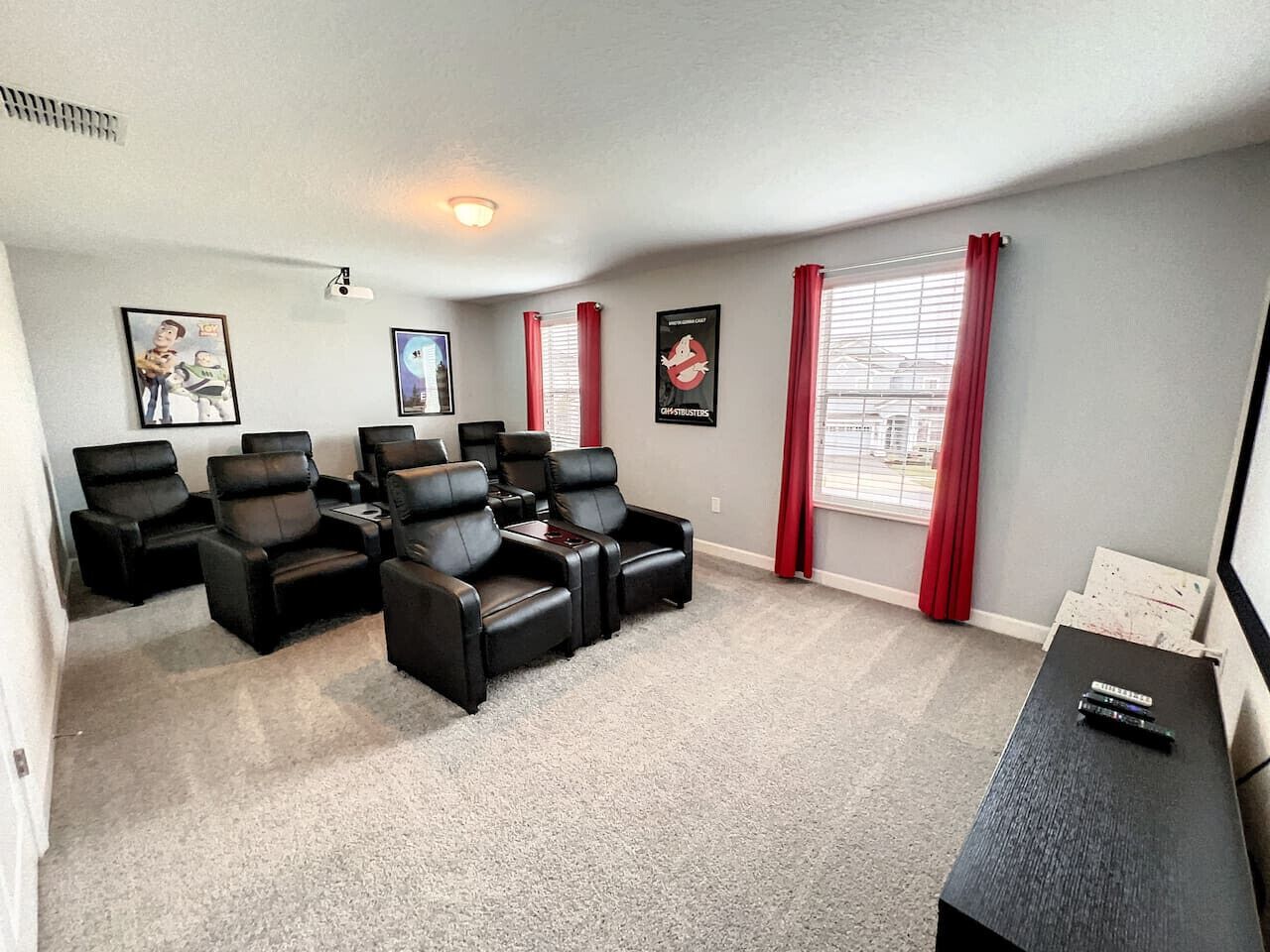 A living room with a carpeted floor, black leather sofas, a coffee table, and a TV stand with remotes.