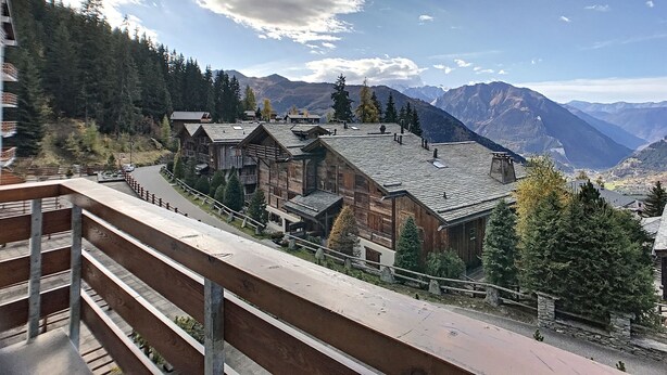 A mountain village with traditional wooden buildings, a paved road, and a view of distant mountains. - Living room with eating area, separate kitchen with dishwasher, one bedroom with 2 single beds, one (Verbier)