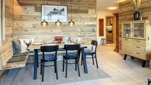 A dining area with a wooden wall, a framed picture, and pendant lights. - Living room with eating area, separate kitchen with dishwasher, one bedroom with 2 single beds, one (Verbier)