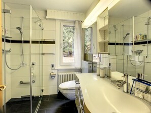 A modern bathroom with a glass shower enclosure, a toilet, a large mirror, and a white sink.