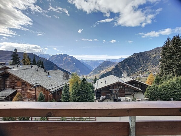A mountain village with wooden houses, a clear sky, and a valley view.