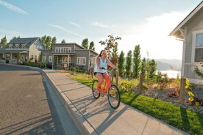 Une rue résidentielle bordée de maisons, une personne à vélo et un ciel dégagé.