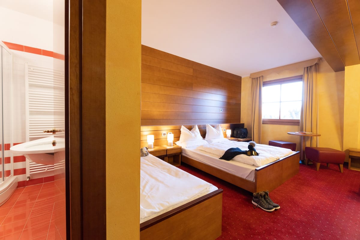 Ein Hotelzimmer mit zwei Betten, einem roten Teppich, einem hölzernen Kopfteil, einem kleinen Tisch und einem Fenster mit Vorhängen.