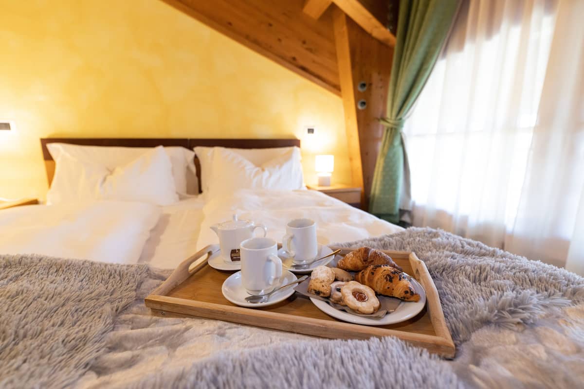 Ein Bett mit weißen Leinentüchern und einem Tablett mit Croissants und Kaffeetassen auf einem flauschigen Teppich.