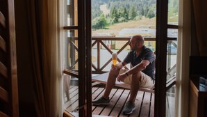 A man sitting on a wooden deck holding a glass of beer, overlooking a scenic view of a forested area. - Hotel Enzo Moro (Sutrio)