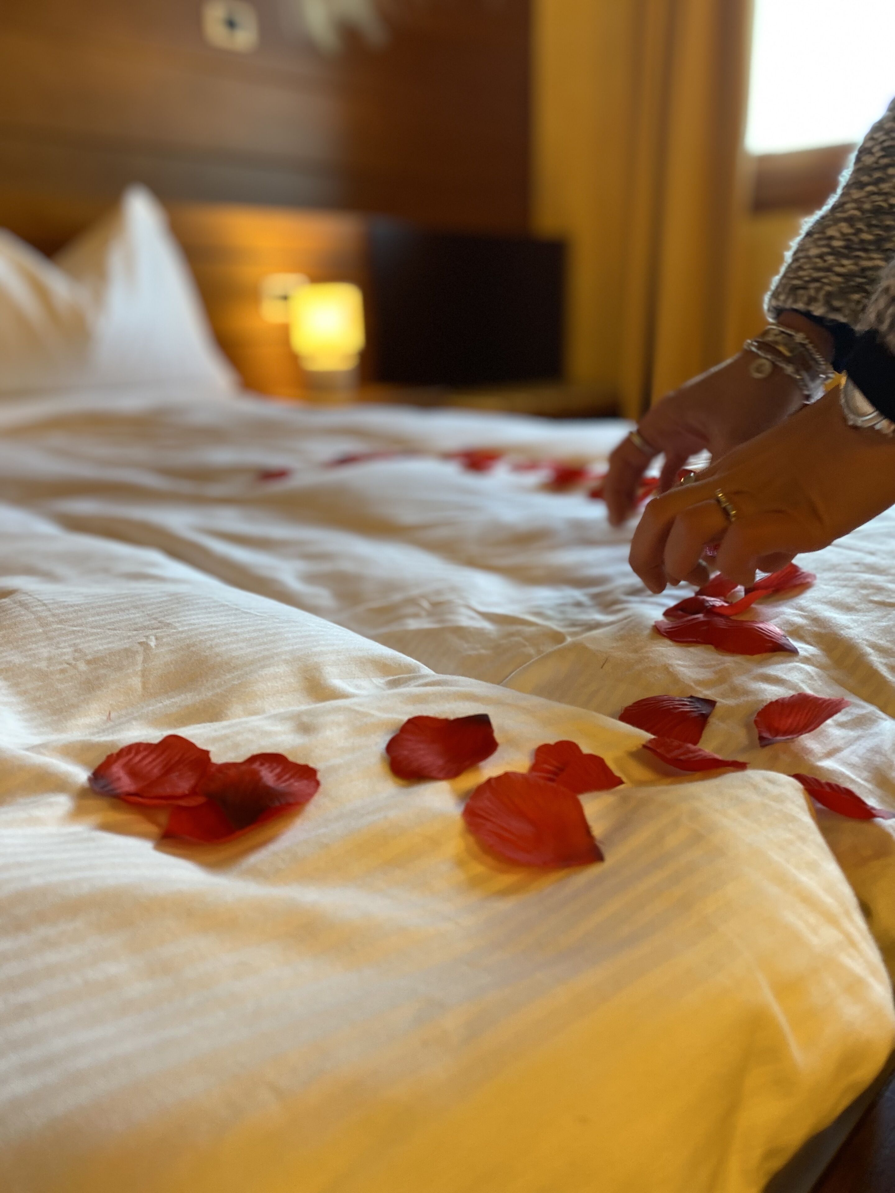 Un letto con lenzuola bianche e petali di rosa rossa sparsi sopra.