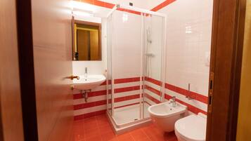 Un baño con ducha envuelta en vidrio, un lavamanos y un inodoro.