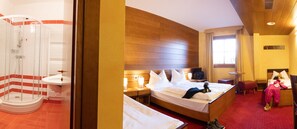 A hotel room with a shower, a bed, a bedside table, a nightstand, a window, and a small seating area. - Hotel Enzo Moro (Sutrio)