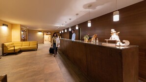 A reception area with a wooden reception desk, a yellow sofa, and a modern light fixture. - Hotel Enzo Moro (Sutrio)