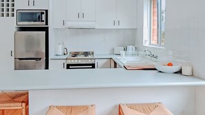 Moderni keittiö, jossa on valkoiset kaapit, ruostumattomasta teräksestä valmistettu jääkaappi, liesi ja pesuallas.