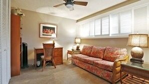 A living room with a wooden desk, a floral sofa, a chair, and a ceiling fan.