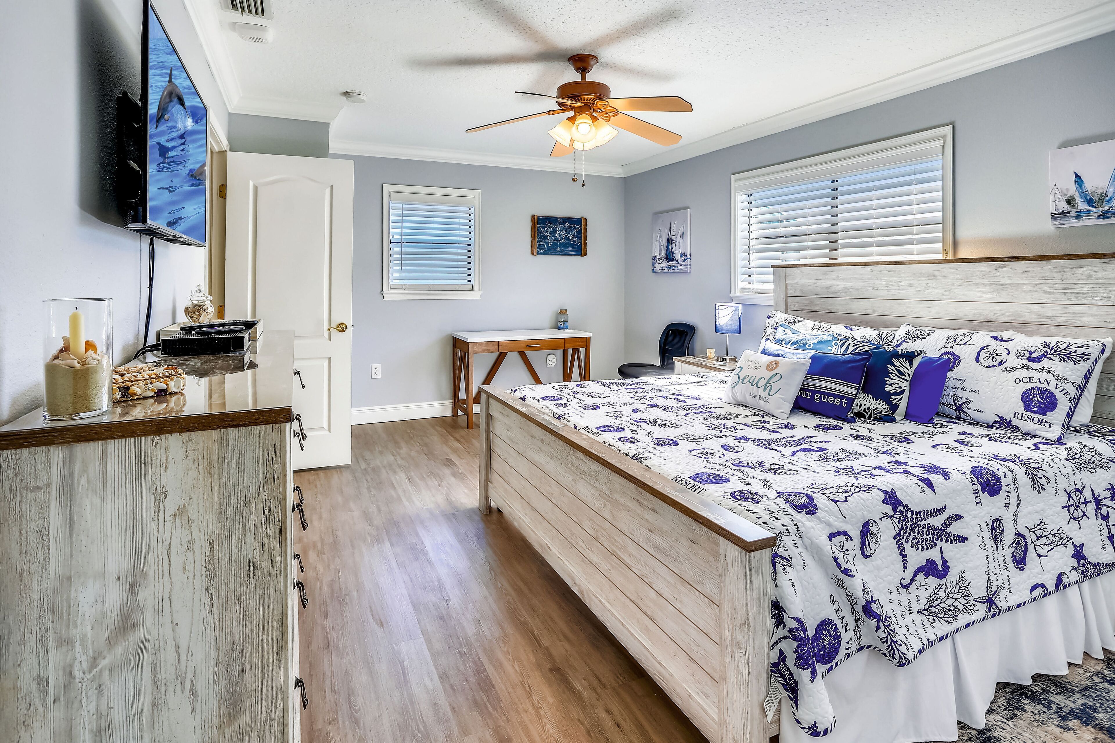 A bedroom with a bed, a ceiling fan, a desk, and a television.