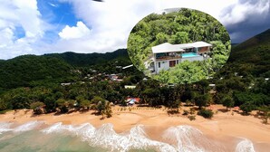 A beach with clear turquoise waters and a sandy shore. There is a house with a pool surrounded by lush greenery. - Villa Zuli (Deshaies)