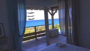 A bedroom with a large bed, a view of the ocean, and a balcony with a railing. - Villa Zuli (Deshaies)