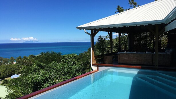 A poolside area with a view of the ocean and a covered seating area. - Villa Zuli (Deshaies)