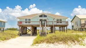 A beachfront house with a wooden deck and a staircase leading to a balcony.
