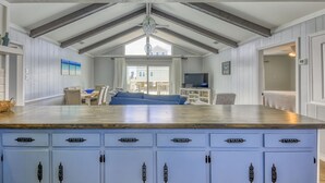 A kitchen with a wooden countertop and blue cabinets, a dining area with a blue sofa, and a large window allowing natural light.