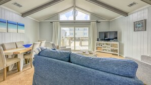 A spacious living room with a large blue sofa, a wooden dining table, and a TV on a white entertainment unit.
