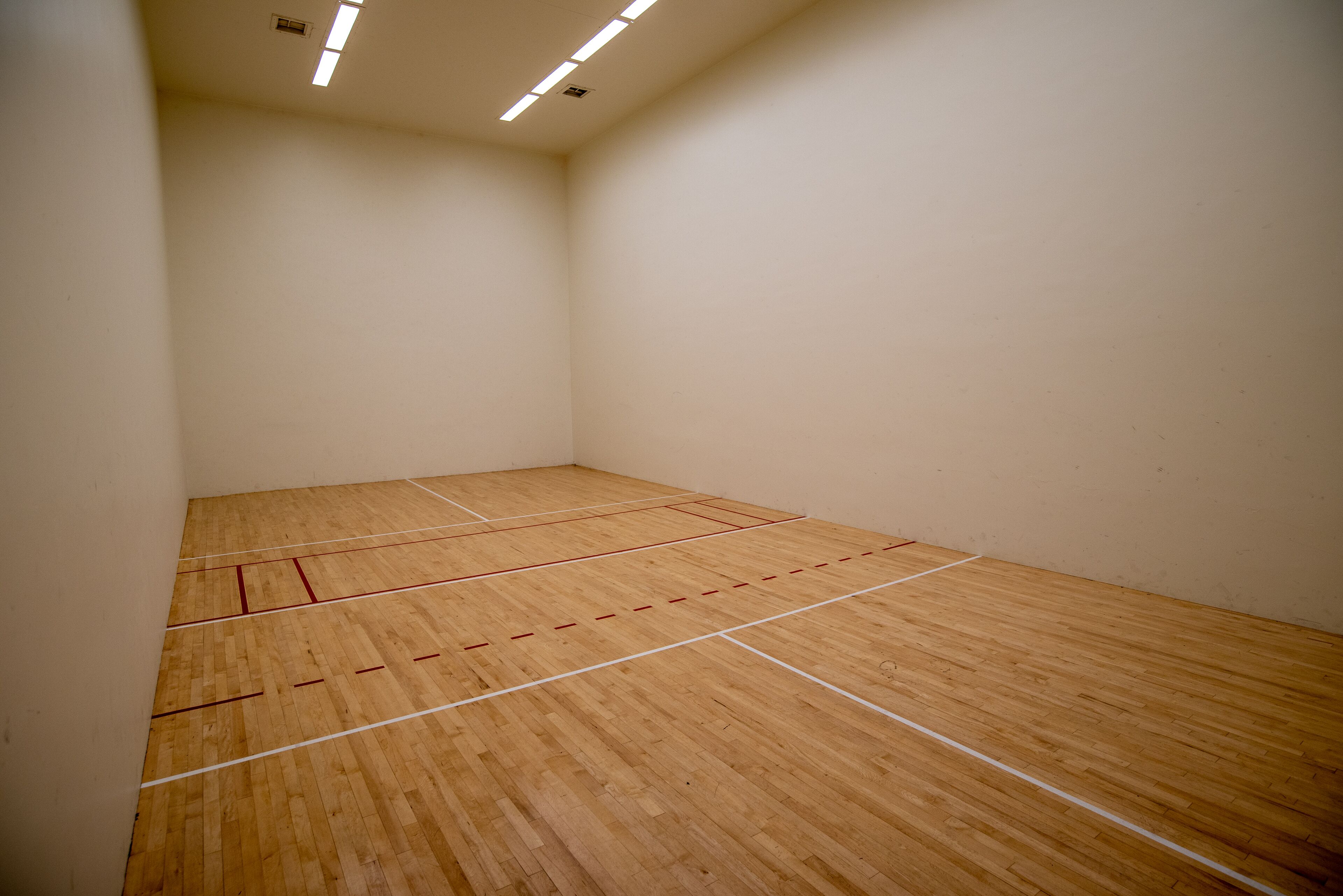 A squash court with wooden flooring and white lines marking the playing area.