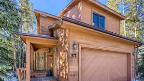Ein zweistöckiges Holzhaus mit Garage, Hausnummer 57, umgeben von Bäumen.