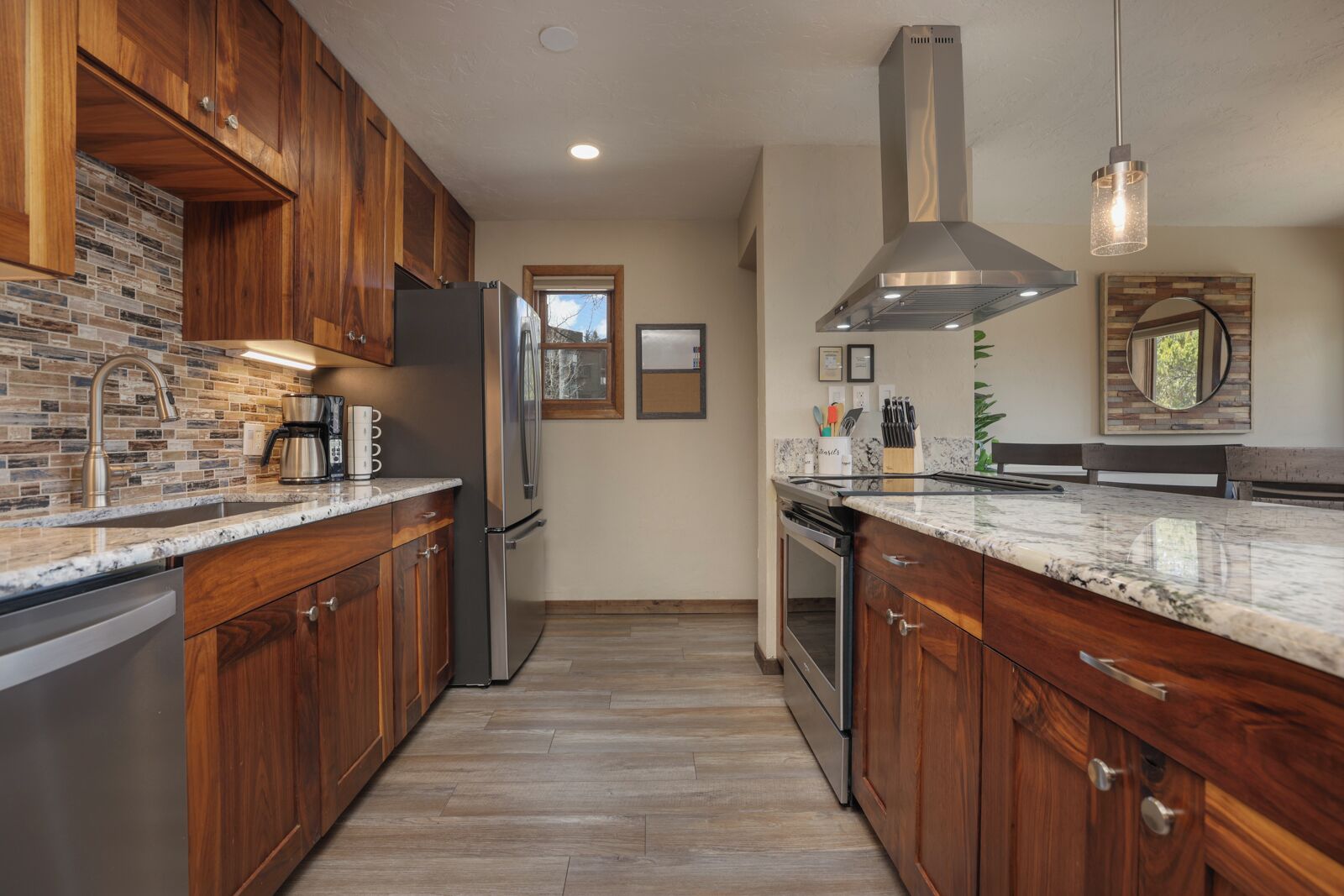 A modern kitchen with wooden cabinets, a stainless steel refrigerator, a built-in oven, and a granite countertop.