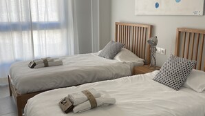 Zwei Einzelbetten mit weißen Leinentüchern, Holz-Kopfteilen und gemusterten Kissen.