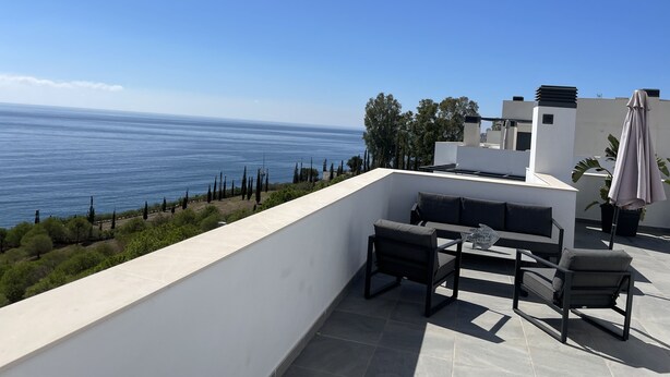 Eine Terrasse mit Meerblick, eine weiße Wand und ein Tisch mit Stühlen.