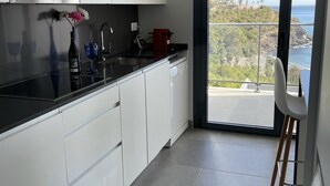 Eine moderne Küche mit weißen Schränken, einer schwarzen Arbeitsplatte und Meerblick durch eine Schiebetür.