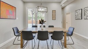 A modern dining room with a wooden table and black chairs, a hanging light fixture, and artwork on the walls. - Trendy and Modern home w/ a Private Pool (Rowlett)