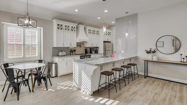 A modern kitchen with white cabinets, a large island with stools, and pendant lighting. - Trendy and Modern home w/ a Private Pool (Rowlett)
