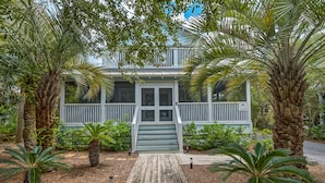A two-story house with a porch, surrounded by tropical plants. - Classic Beach Home - Heated Private Pool, Sleeps 11 +Free Attraction Tickets! (Santa Rosa Beach)