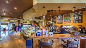 A coffee shop interior with a counter, bar stools, a display case with pastries, and a menu on the wall. - Beautiful Oceanfront Corner Unit - Honua Kai 215 (Lahaina)
